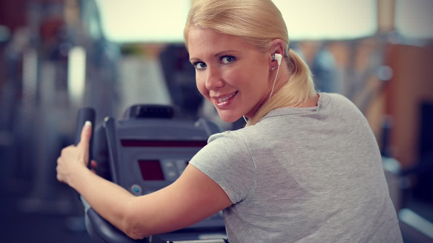 Happy woman in gym on a hometrainer listening to music