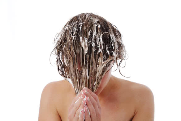Woman with her wet soapy hair covering her face washing and conditioning it with bare shoulders