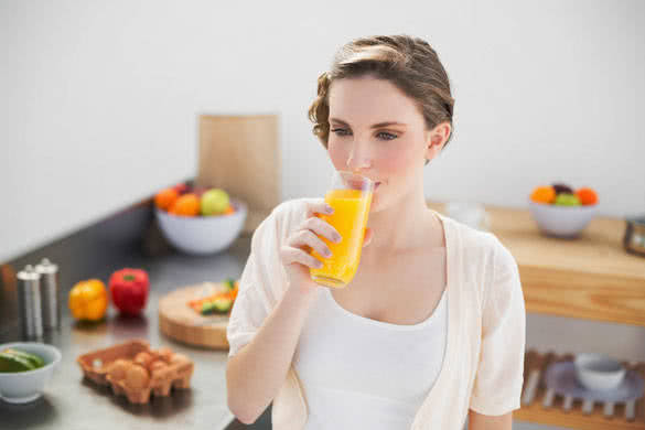 Lovely brunette woman drinking a glass of orange juice standing in her kitchen at home