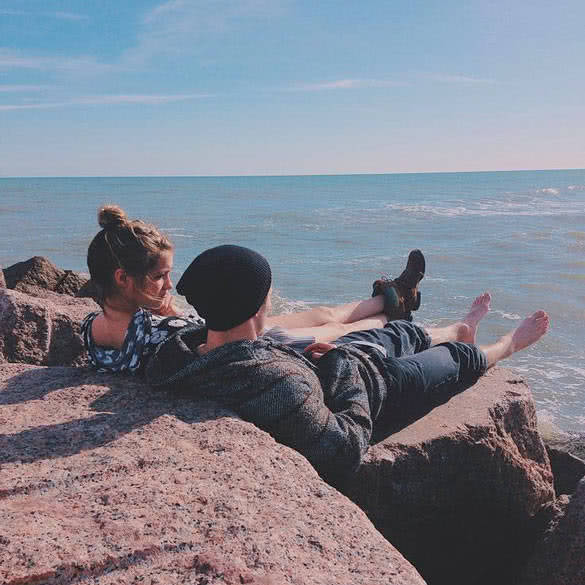 couple sitting on the rock and looking at the sea