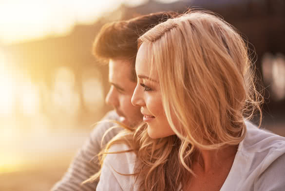 pretty girl cuddling with boyfriend on beach at santa monica with shallow depth of field and bright warm lens flare