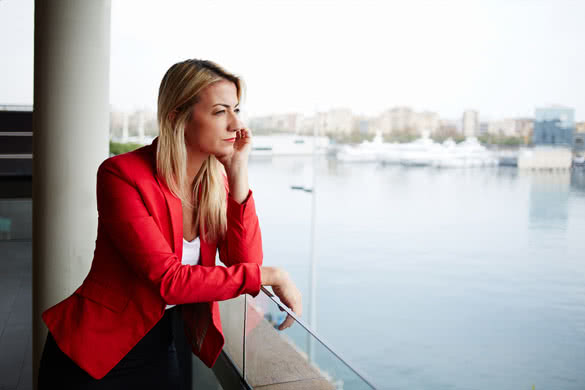 Portrait of pensive businesswoman looking out of an office balcony with beautiful seaport view on background