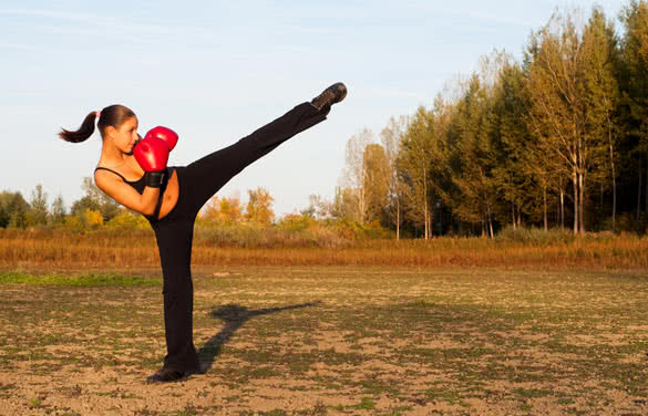 Beautiful kick boxing girl exercising high kick in the nature on sunny summer day