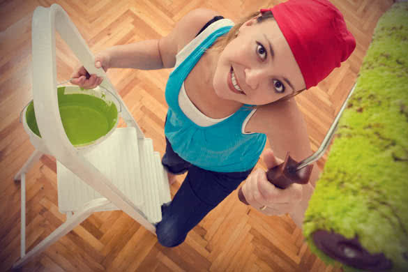 Happy woman painting the ceiling green standing on a ladder