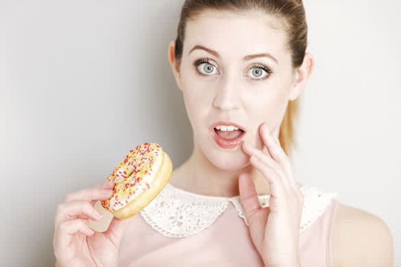 Young woman deciding whether to eat an unhealthy doughnut expressing guilt