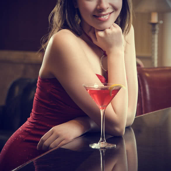 adult woman in red dress smiling and standing at bar with drink
