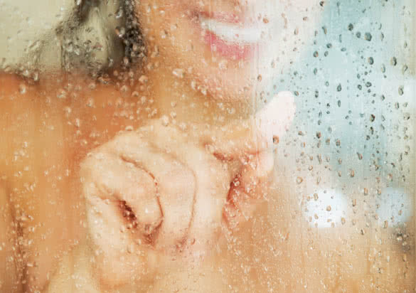 happy young woman drawing heart in weeping glass shower door