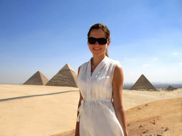 happy young woman standing in front of egyptian pyramids in giza