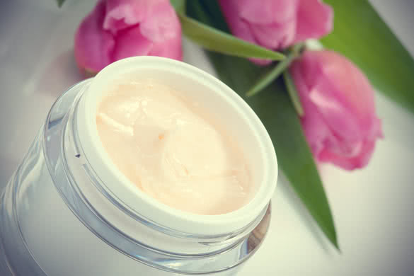 jar of moisturizing face cream surrounded by pink tulip flowers