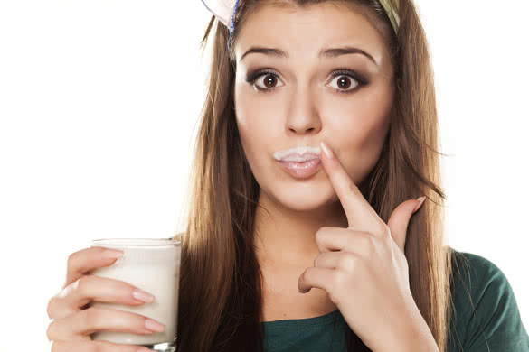 pretty happy girl in a green shirt with a pleased gesture drinking milk and wiped her mouth with a finger