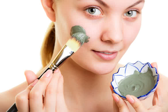 Woman applying with brush clay mud mask on face
