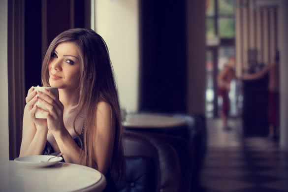 pretty young woman sitting in the cafe with a cup of tea