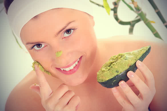 young woman applying natural avocado mask on her face