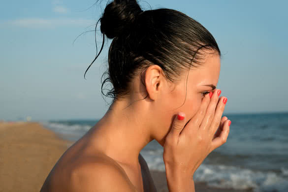 young woman rubbing irritated sensitive eyes on the beach