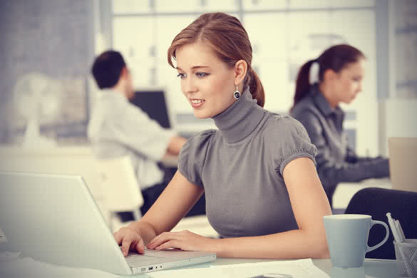 Young woman working in office, sitting at desk using laptop
