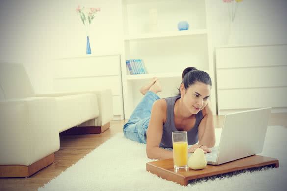 Happy woman lying on floor at home and working on laptop computer