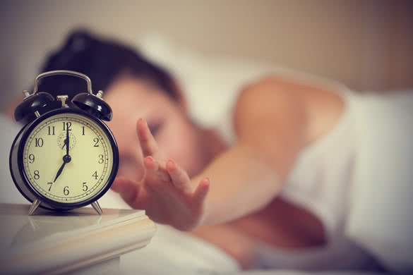 Woman lying in bed turning off an alarm clock in the morning at 7am