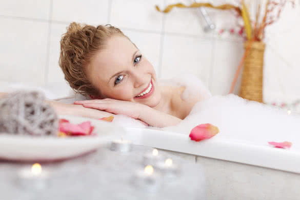 Beautiful woman relaxing in a foamy bubble bath resting her head on the side and smiling