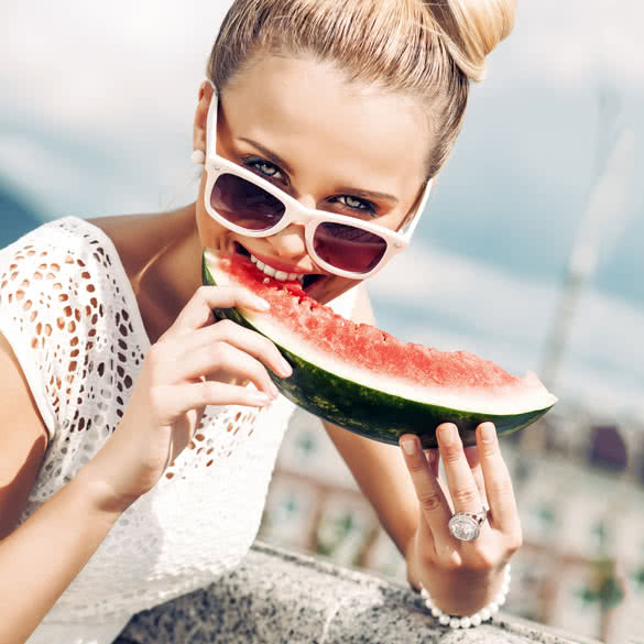 beautiful young girl with bow tie hair in white summer dress wearing sunglasses bites juicy watermelon