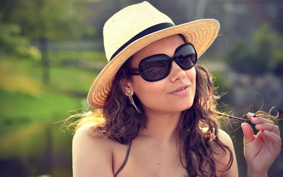 closeup portrait of a brunette woman wearing a nice summer beach hat and sunglasses