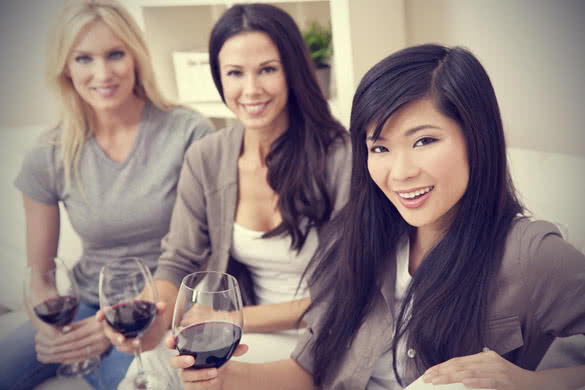 three beautiful young women friends at home drinking red wine together