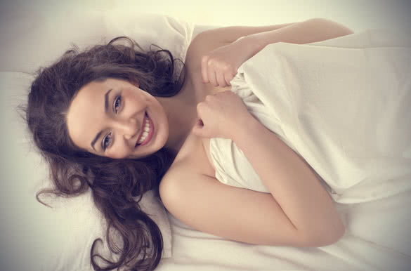 portrait of happy woman lying on white silk bed