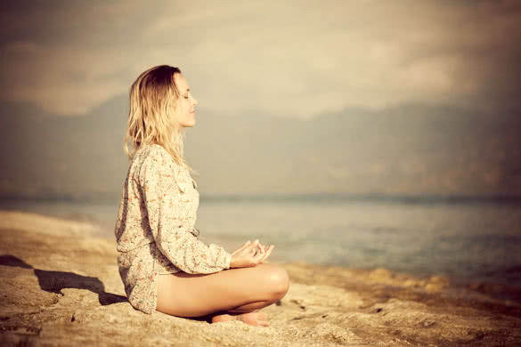 Woman sitting in lotus position on rock by the sea