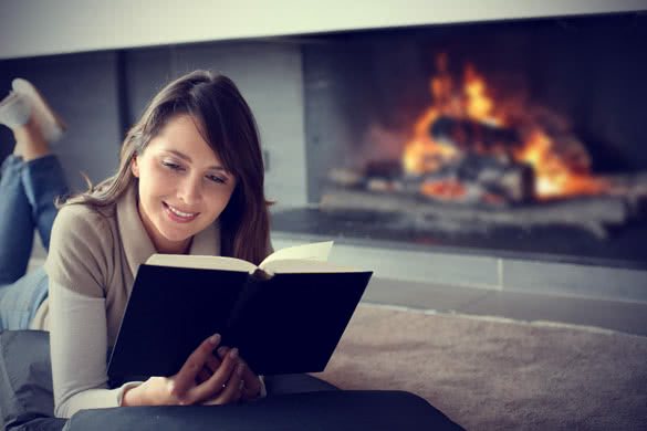 woman reading book next to a fireplace