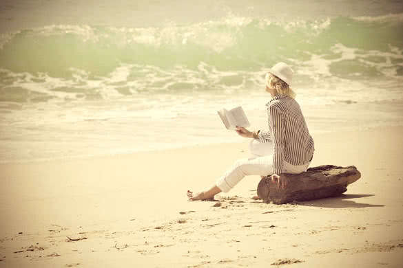 woman with hat reading book on the beach