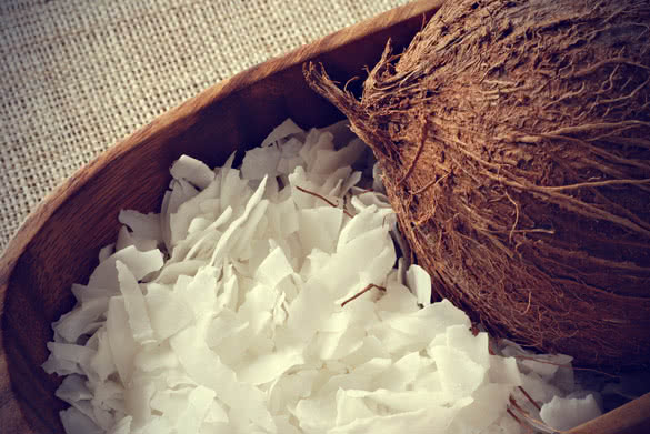 Coconut flakes with whole coconut in wooden bowl