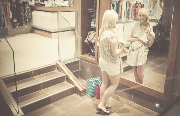 Woman looking in the mirror holding clothes in the shop