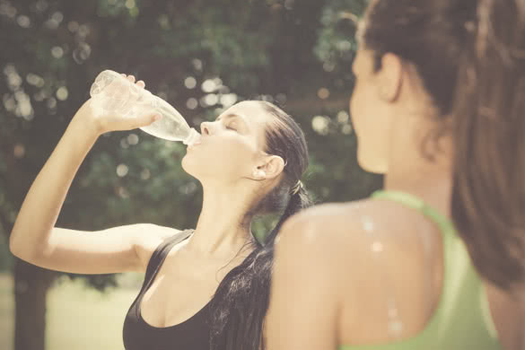 Two female friends relax and drinking water after running in city park