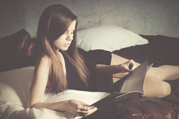 Young woman on the bed reading a magazine