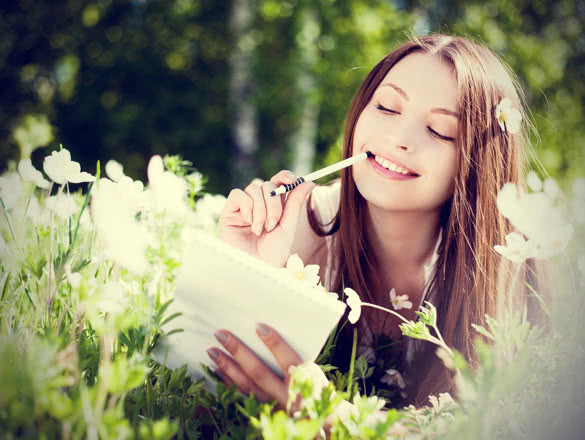 young brunette woman writing in her diary on the meadow with white flowers