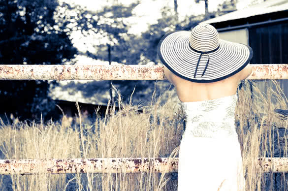 back of a Woman wearing a big hat leaning on a rusted fence