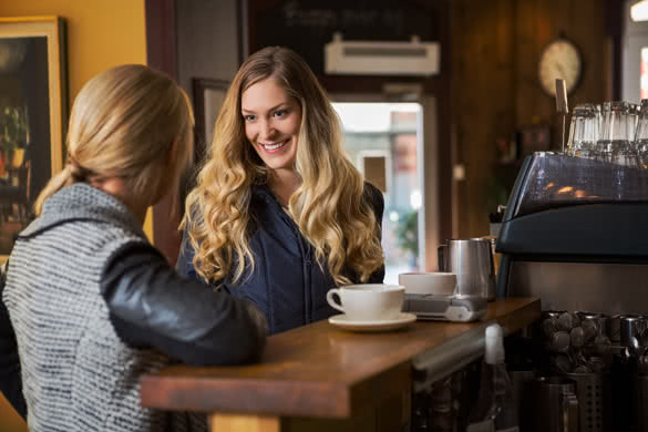 happy female friends having a conversation by counter in coffeeshop