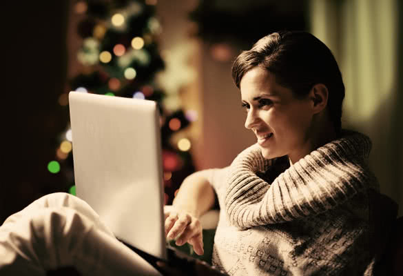 Happy young woman working on laptop in front of christmas tree