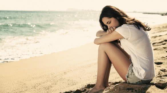 Portrait of a worried girl sitting on the beach with the sea in the background