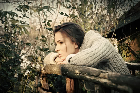 beautiful woman leaning chin on old wooden fence thinking