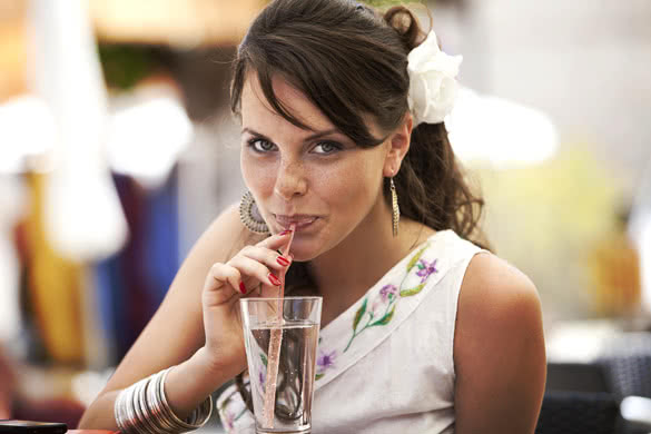 girl drinks water from a glass through a straw
