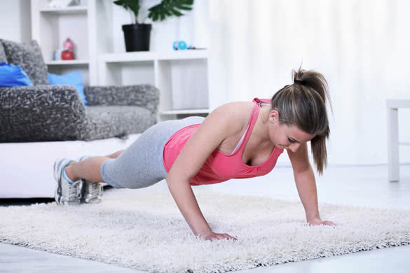 Young woman looking down while doing push-ups in living room