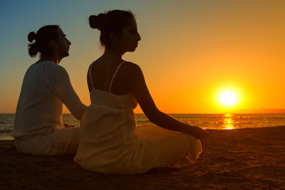 couple doing yoga exercises on a beach at sunrise
