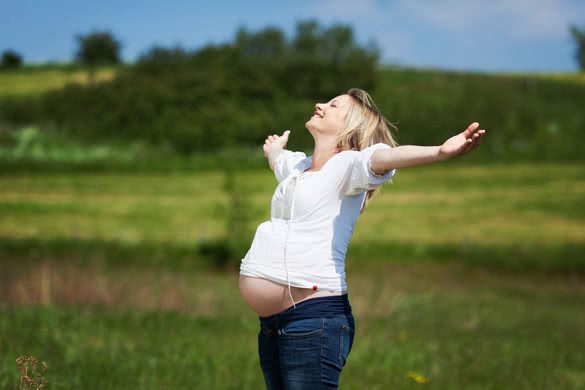 Happy pregnant woman with arms outstretched enjoying sunlight at field
