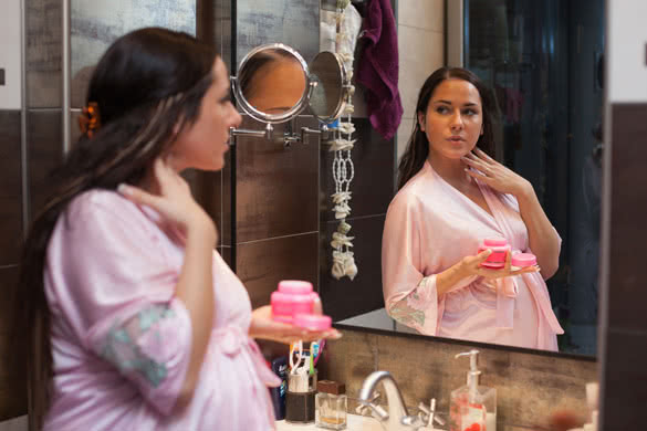 Young pregnant woman with cosmetic cream in a bathroom