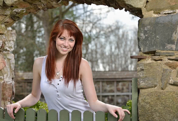 woman with red hair  smiling outside at a fence doorway