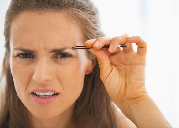 Displeased young woman tweezing eyebrows