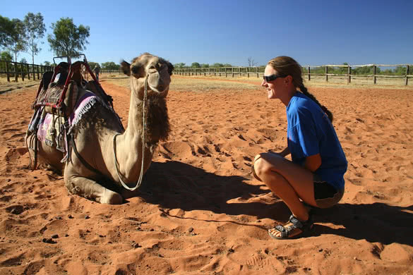 Cheerful young woman kneeling by the camel