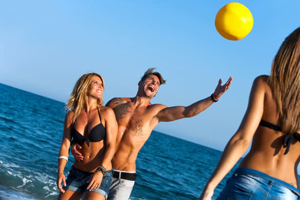 Group of friends having fun with inflatable ball on beach