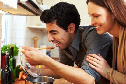 Man tasting soup on a stove in kitchen while happy woman is watching