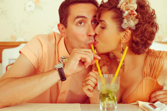 Portrait of a beautiful married couple of hipsters in trendy clothing drinking mojito and kissing in vintage cafe